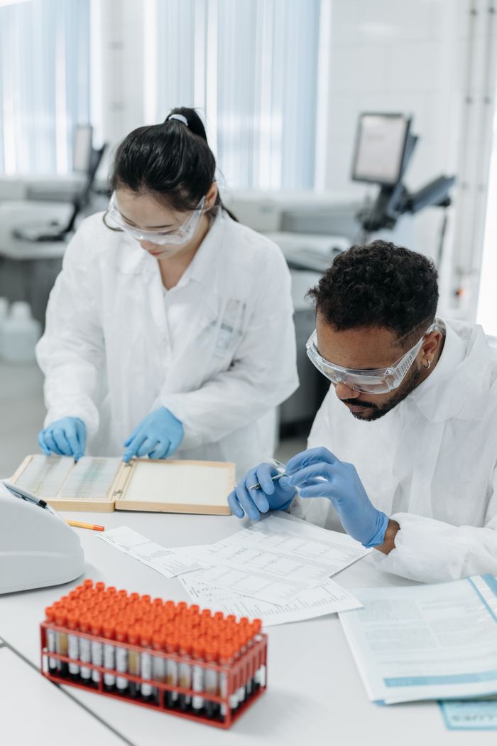 Two scientists in protective gear analyze samples in a modern laboratory setting.